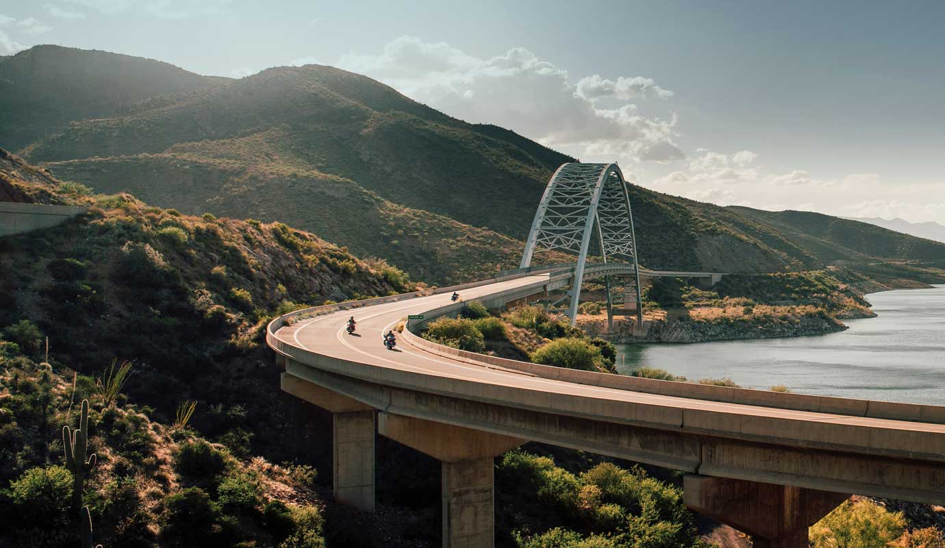 A curving road bridge between a body of water and hills