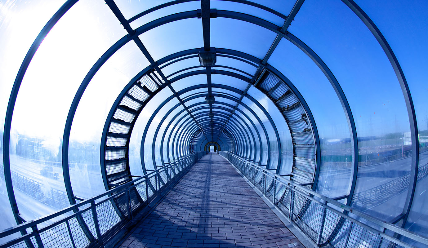 A view down a circular glass tunnel over a highway